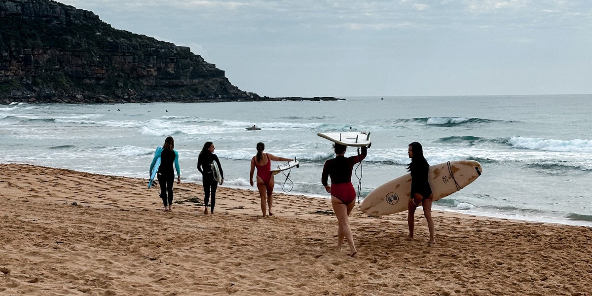 women walk into water together with surf boards