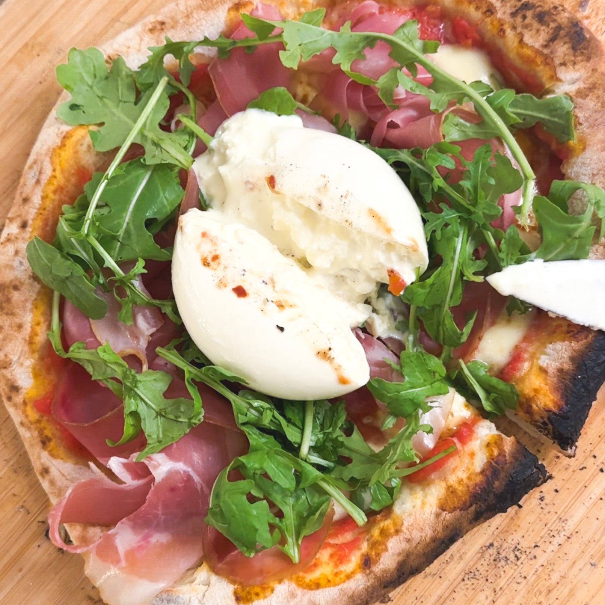 Pizza with arugula, prosciutto, and a burrata on a wooden board