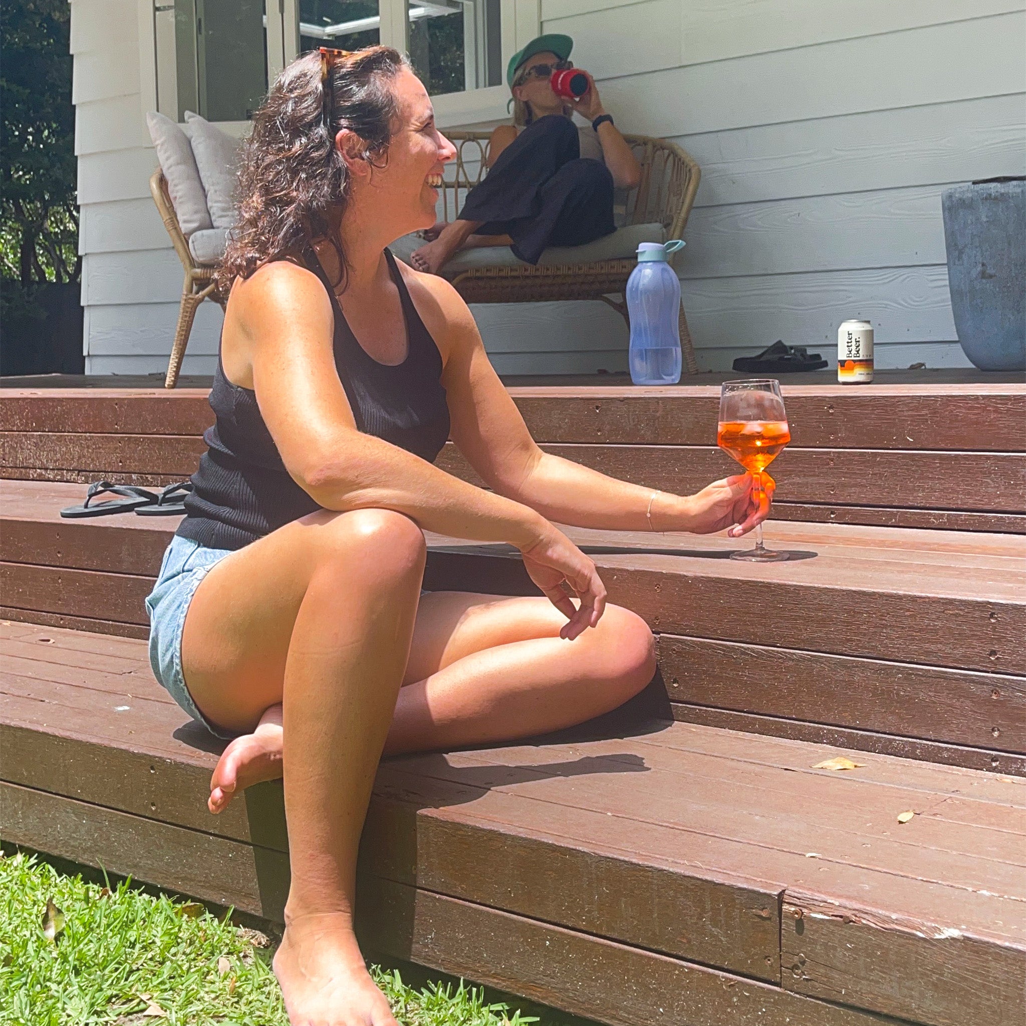 Woman sitting on wooden steps holding a glass of aperol spritz, with another person in the background.