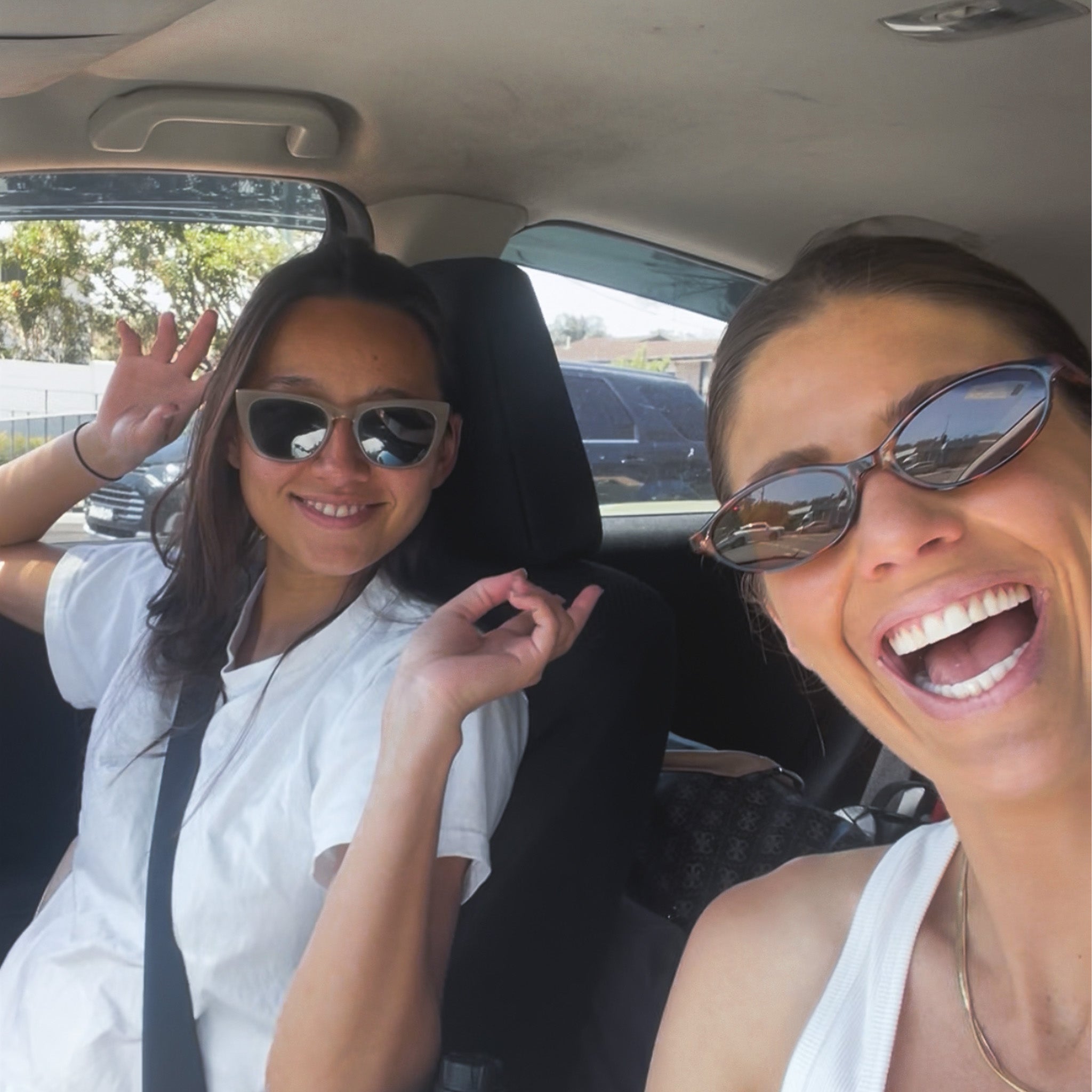 Two women in a car, wearing sunglasses and smiling.
