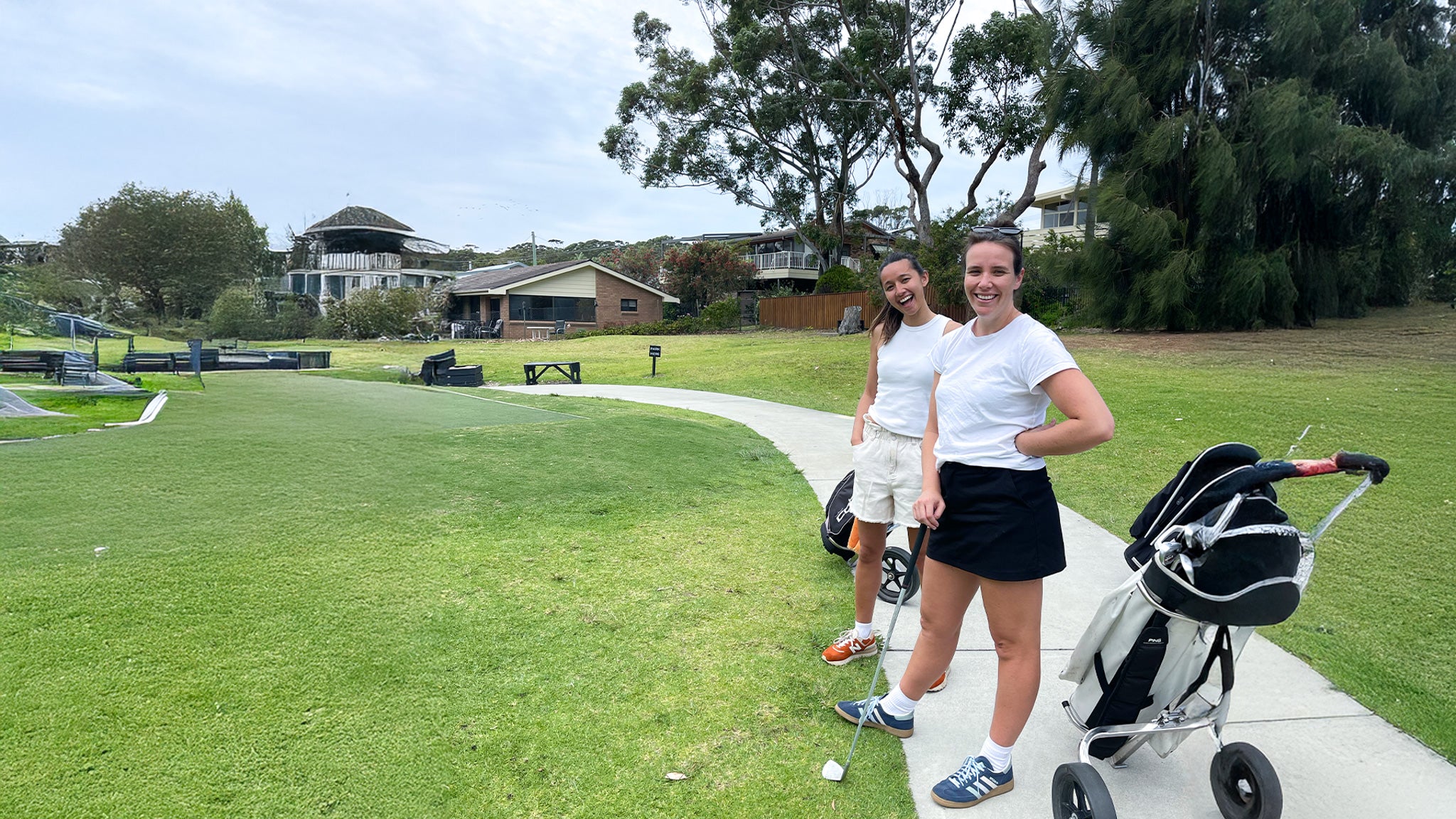 Two women standing on a golf course with golf trolleys.
