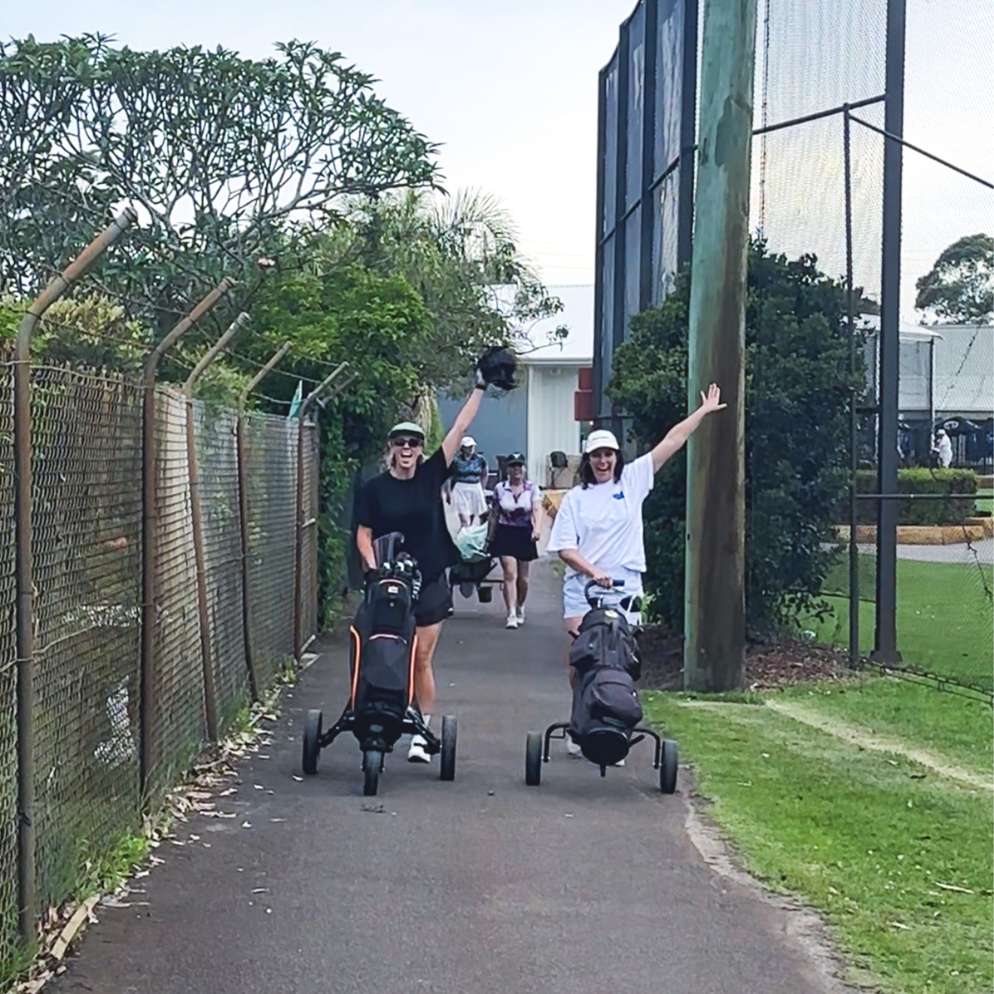 Two people with golf trolleys on a path in a in a golf course