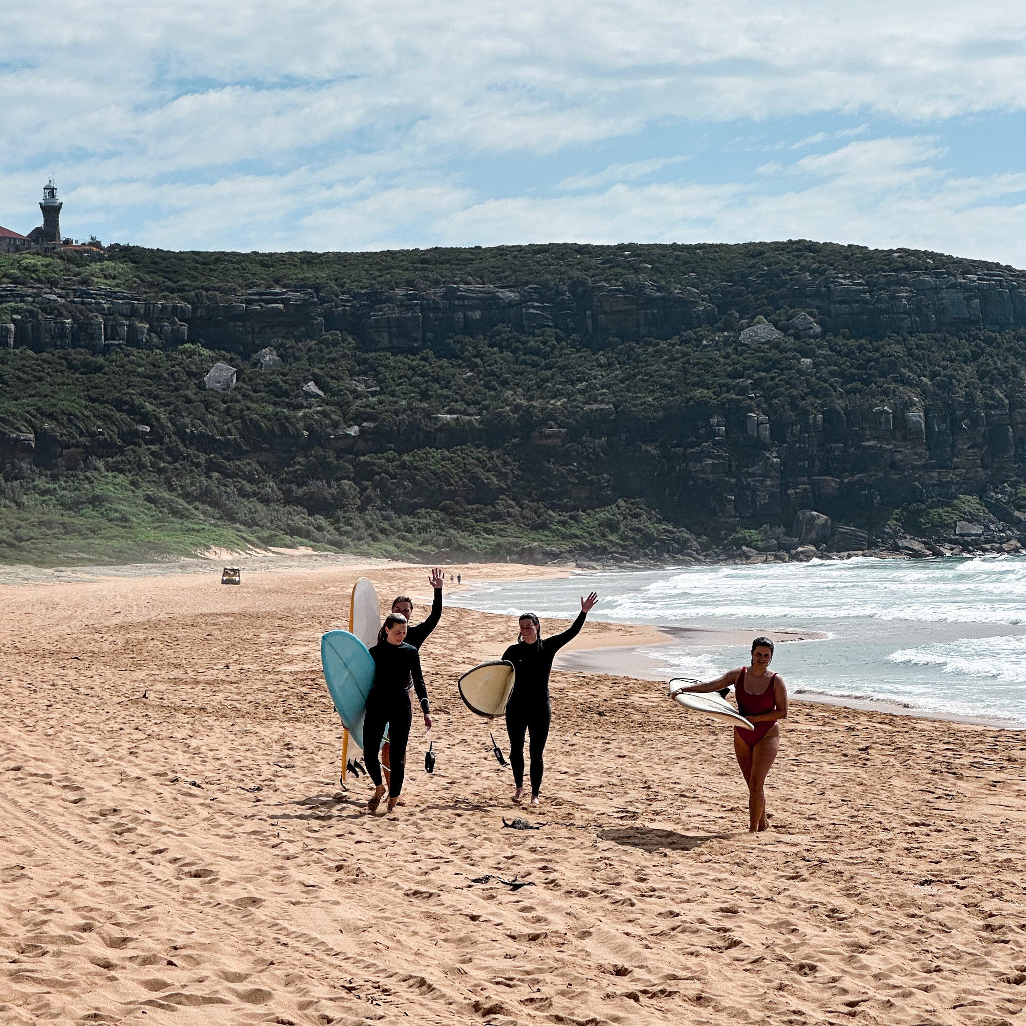 Three people with surfboards walking on a beach with a lighthouse in the background
