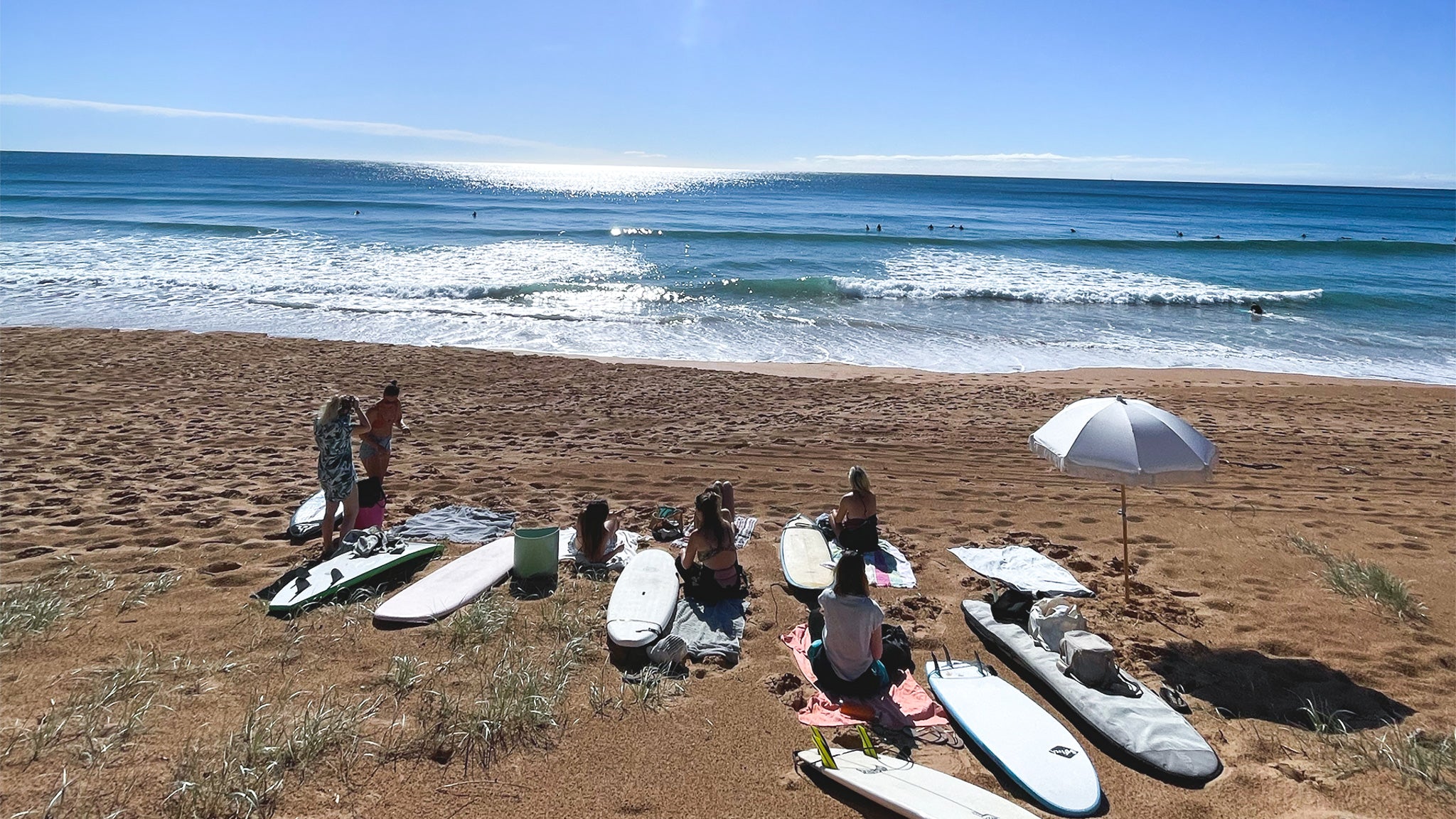 People with surfboards on a sandy beach under a clear blue sky